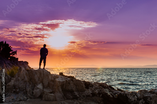 Yung man standing on a rock and looking at the sea sunset