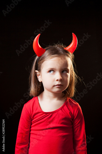 Studio shot of a Cute 5 years old girl with a red devil costume against black background