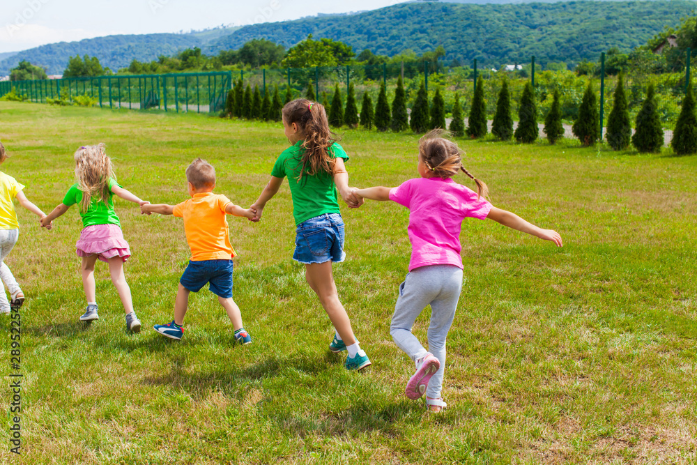 Children play holding hands on the green grass, back view