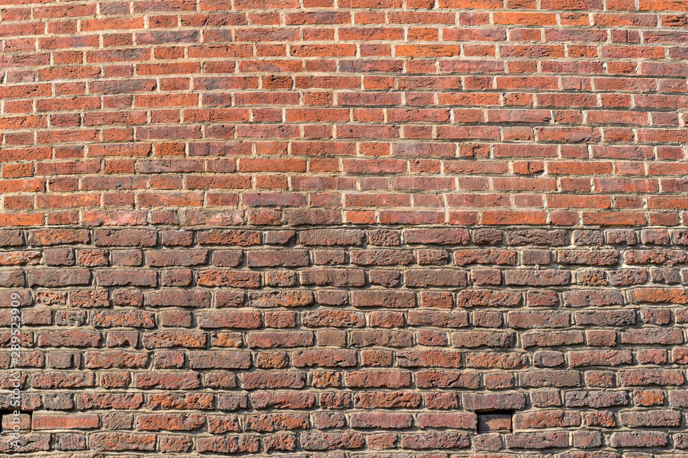 Naklejka premium Old brickwork. The wall is made of red brick. The upper part of the wall is a lighter color. The bottom of the wall is darker in color.