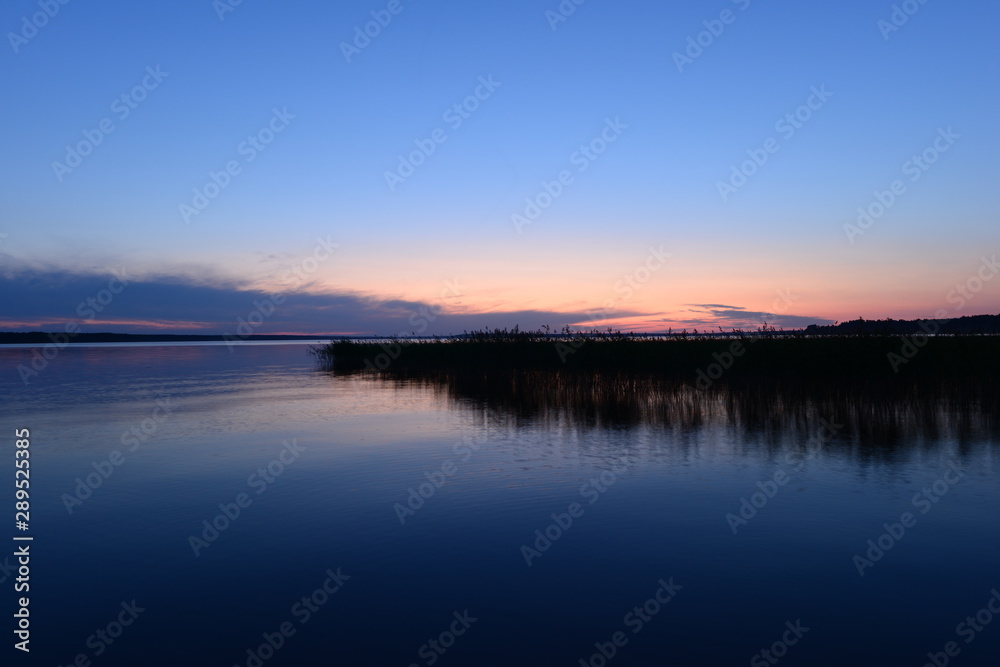 Calm cloudless blue sky over the lake in the twilight glow in the night silence