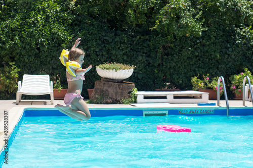 Happy little girl jumps in the pool  summertime background with copy space © hiddencatch