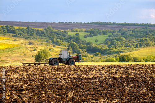 An agricultural tractor plows a field with a plow after harvesting wheat in the rays of the evening sun.