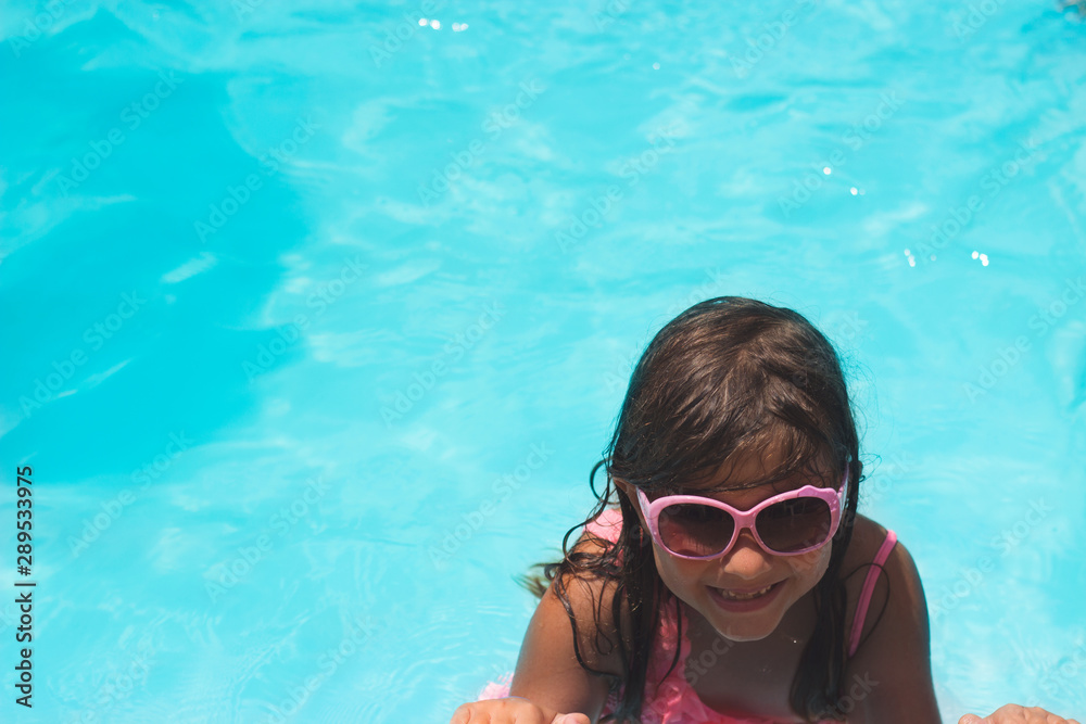 Little girl with sunglasses smiling in the swimming pool