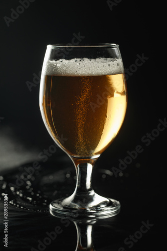 glass of beer with foam on wet surface isolated on black