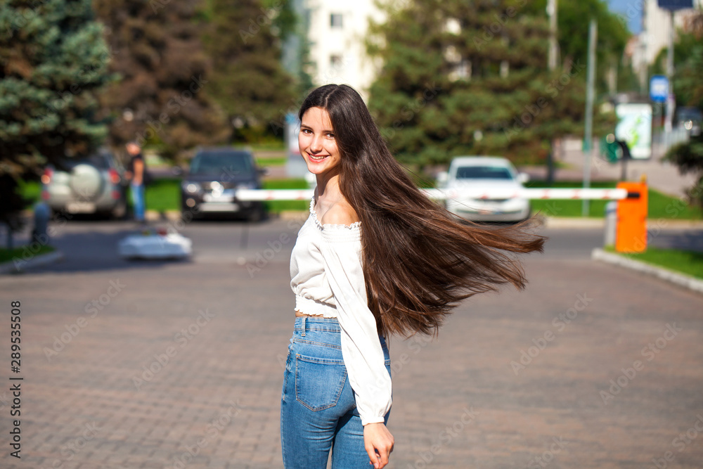 Young beautiful brunette woman in jeans and white blouse walking in summer street Young beautiful brunette woman in jeans and white blouse walking in summer street