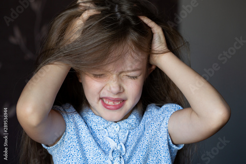 the girl is crying, grabbed her head, a child’s problems. The girl scratches her head, severe itching, infection with lice photo