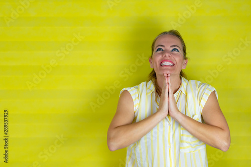 Woman wearing yellow and white striped shirt on isolated background praying with hands together asking for forgiveness smiling confident.