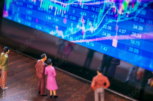 Financial graphics on screen while miniature people are following them