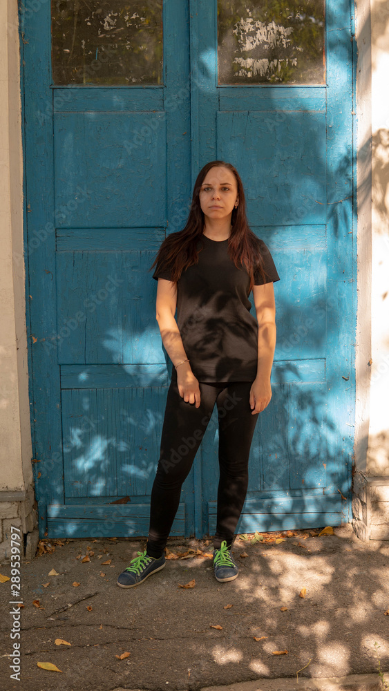A young woman in a black t-short with long hair on the background of an old building with blue doors. A young woman in a black t-short with long hair on the background of an old building with blue doors.