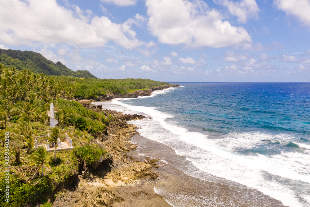 The rocky coast of a tropical island. Siargao, Philippines. Seascape with palm trees in sunny weather, aerial view.