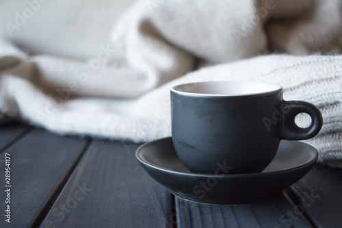 Close-up black cup with coffee on gray knitted sweater made of natural wool texture, wavy folds, selective focus