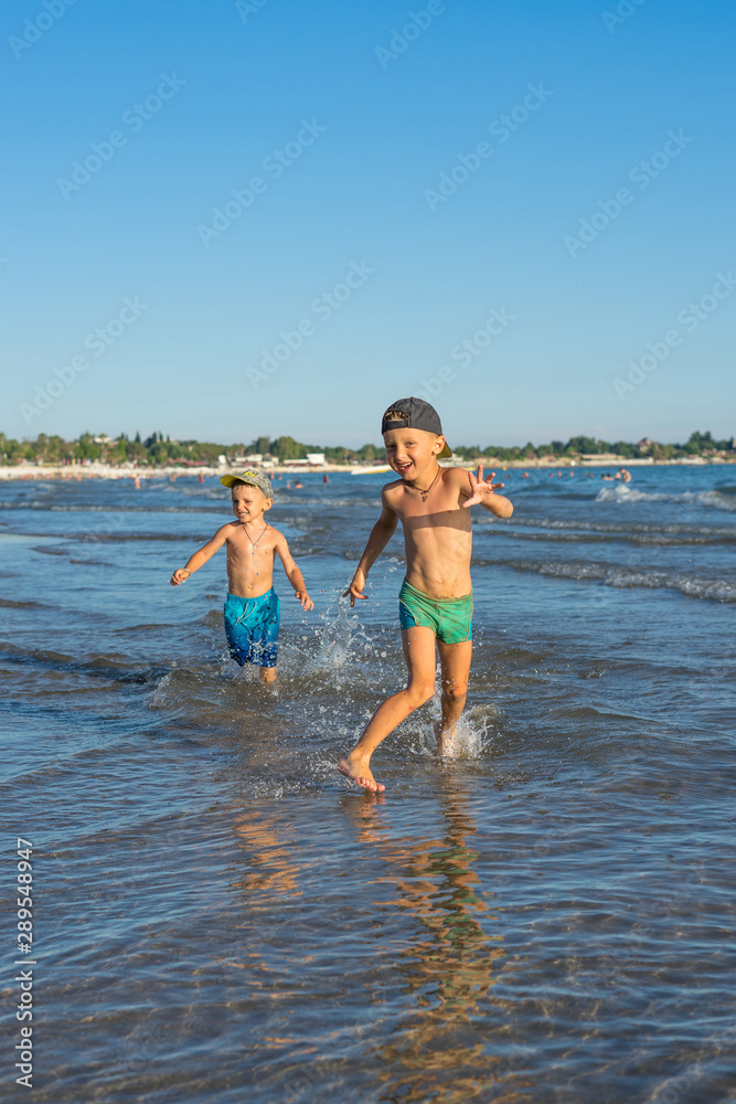 Happy barefoot family having fun – two brothers together run with splashes by water pool along surf of sunset sea beach. Active parents, people activity on summer holiday with children.
