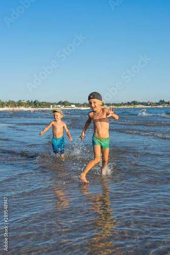 Happy barefoot family having fun – two brothers together run with splashes by water pool along surf of sunset sea beach. Active parents, people activity on summer holiday with children. © Evgenia