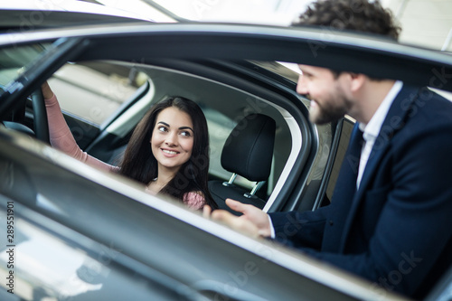 Elegant woman sitting in car and listening to salesman in automobile center