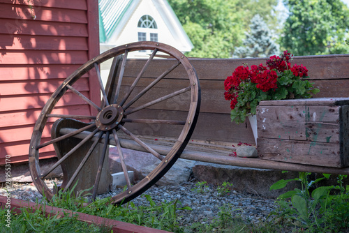 Old Rustic Wagon Wheel leaning on Bench outside a Red Barn