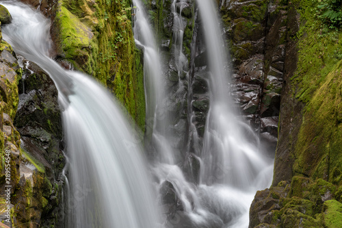 Multiple long exposure waterfalls into green forest canyon.