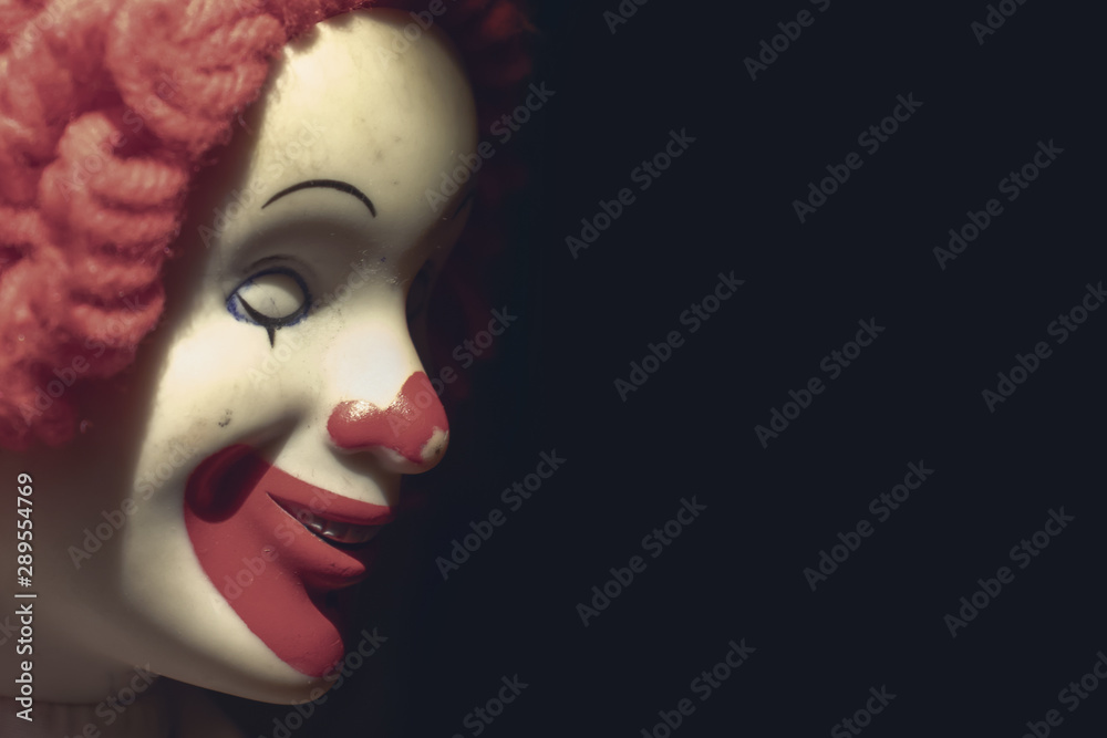 Scary evil sinister clown face with a spooky smile on black background with copy space, coulrophobia and fears concept