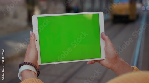 Close up hands woman using tablet device computer with green screen outdoors in street at sunlight background tram message pad technology chroma key female digital girl app chat finger slow motion