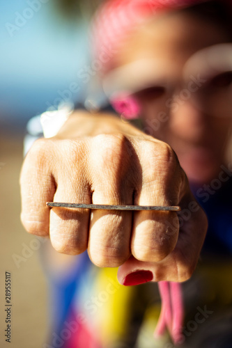 Closeup on pinup woman showing punch sign on her hand wearing red nail polish, rings, bracelets and sunglasses, colorful image retro style