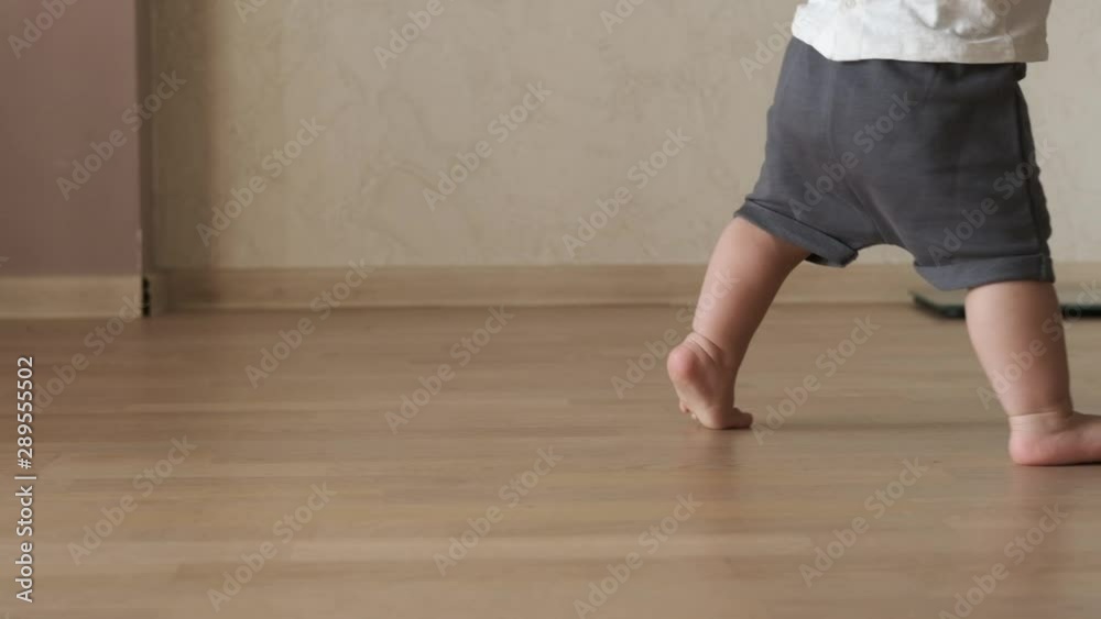 Closeup of baby tiny barefoot legs doing first steps and walking on floor at home without any help. Slow motion Closeup of baby tiny barefoot legs doing first steps and walking on floor at home without any help. Slow motion