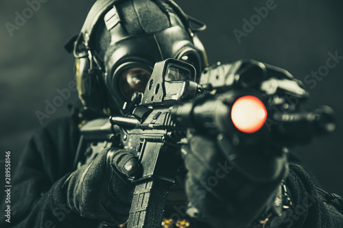 Elite special unit soldier with gasmask is holding assault rifle and aiming at the target