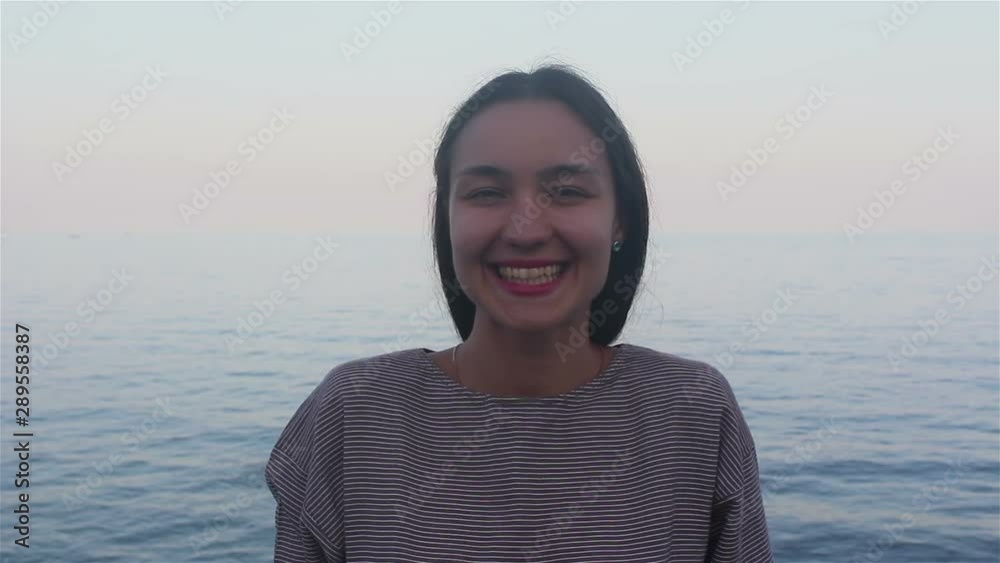 Close-up portrait of an attractive girl on a background of the sea, she is looking at the camera and smiling.Portrait of a young beautiful girl on the background of the blue sea. Close-up portrait of an attractive girl on a background of the sea, she is looking at the camera and smiling.Portrait of a young beautiful girl on the background of the blue sea.