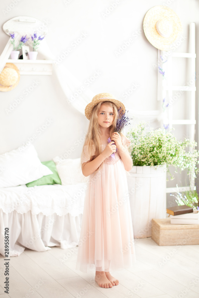 little girl in a straw hat and dress holds a bouquet of lavender in a children's room in a white bedroom with a rustic interior. Childhood concept. Provence style bedroom, room interior. Aromatherapy
