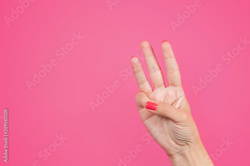 Closeup view of beautiful manicured white female hand isolated on bright pink background. Woman raising three fingers up. Horizontal color photography.