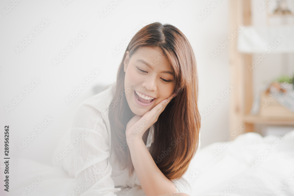 Young Asian woman lie on the tummy on white bed and looking down which smiling and felling happy at home. the life of woman at family home concept. Young Asian woman lie on the tummy on white bed and looking down which smiling and felling happy at home. the life of woman at family home concept.