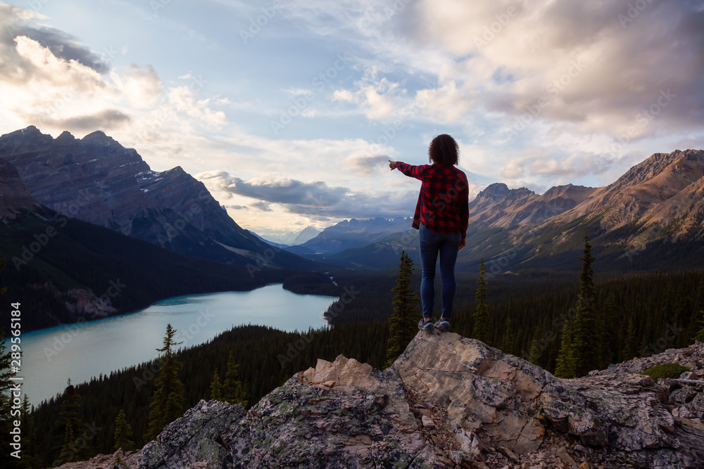 Adventurous girl with open arms standing on the edge of a cliff overlooking the beautiful Canadian Rockies and Peyto Lake during a vibrant summer sunset. Taken in Banff National Park, Alberta, Canada. Adventurous girl with open arms standing on the edge of a cliff overlooking the beautiful Canadian Rockies and Peyto Lake during a vibrant summer sunset. Taken in Banff National Park, Alberta, Canada.
