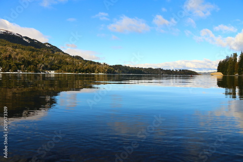 lago de aguas cristalinas y reflejo perfecto, rodeado de bosques de pinos y barcos flotando, en Bahia Manzano cerca de Villa La Angostura, Patagonia Argentina