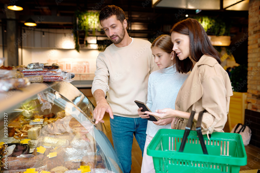 Contemporary family of three choosing meat products in supermarket