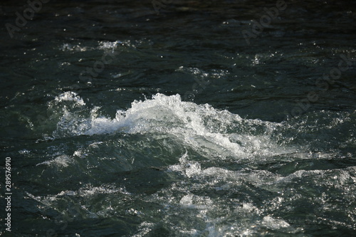 Closeup of fast flowing stream. Bubbles and foam on water surface,
