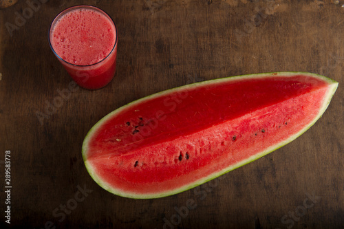 Watermelon smoothie in a glass and half of the long, green watermelon, with stripes from above
