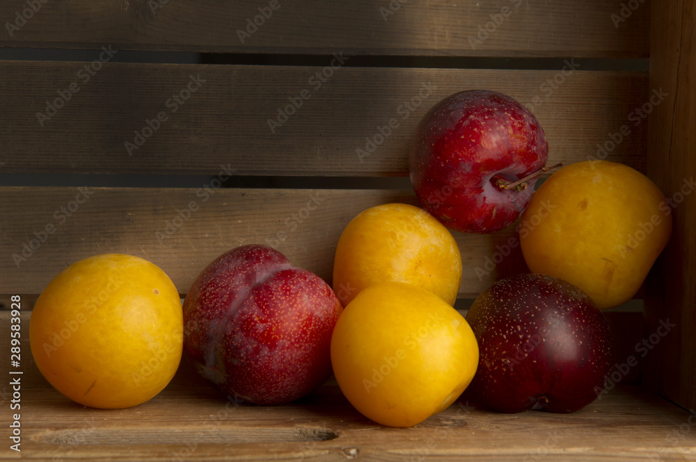 Many yellow and red plums in a wooden fruit box Many yellow and red plums in a wooden fruit box