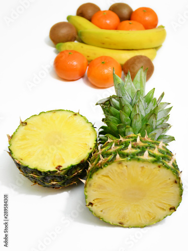 An image of a half-cut pineapple on a background of several bananas, mandarins and kiwis on a white background