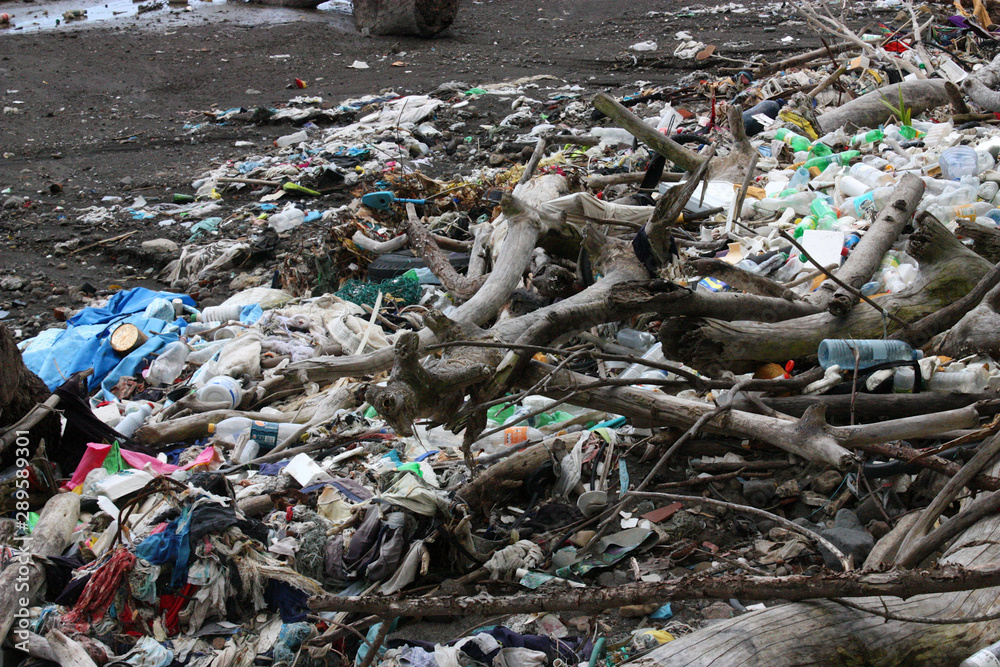 Obraz premium Huge messy pile of plastic and trash litter among wood branch debris polluting bare brown sand beach environment near ocean