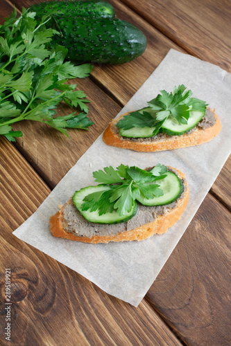 Delicious sandwiches for a snack on the board. Slices of white bread with sprat paste, cucumber and parsley. Cold appetizer on a vintage wooden table. 