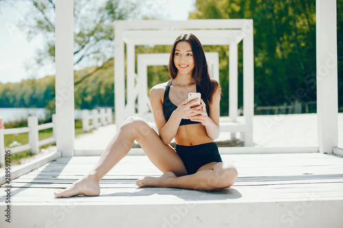 Pretty lady sitting on a summer beach. Girl use the phone; Brunette in a black swimsuit