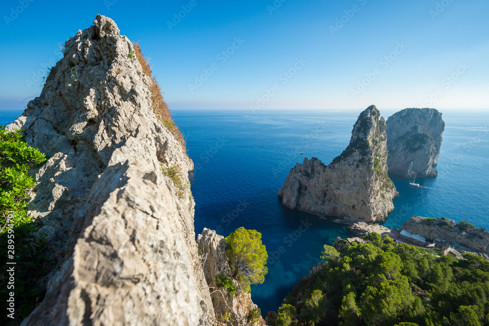 Bright scenic view of the iconic Faraglioni rocks from the nearby cliffside trail on the Mediterranean island of Capri, Italy
