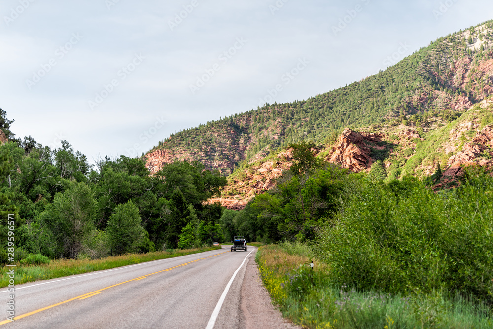 View of rocky red cliff from road Highway 133 in Redstone, Colorado during summer with trees in evening sunlight and cars