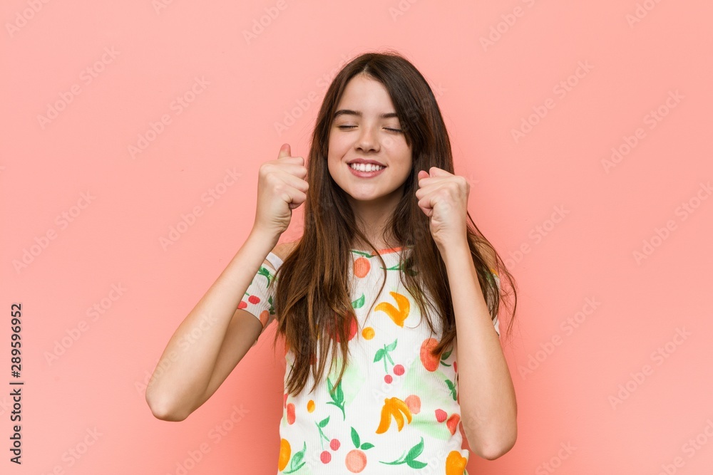 Girl wearing a summer clothes against a red wall raising fist, feeling happy and successful. Victory concept. Girl wearing a summer clothes against a red wall raising fist, feeling happy and successful. Victory concept.