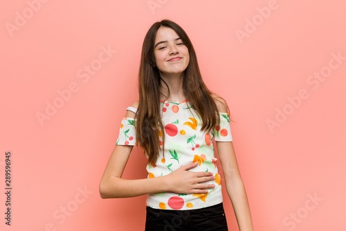 Obraz na płótnie Girl wearing a summer clothes against a red wall touches tummy, smiles gently, eating and satisfaction concept