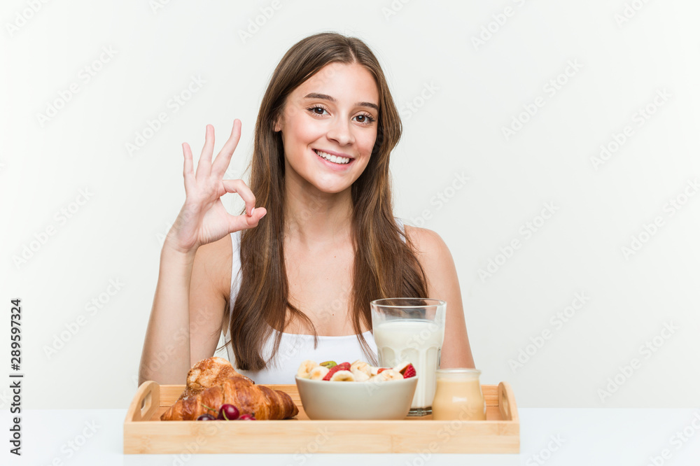 Young caucasian woman having breakfast cheerful and confident showing ok gesture. Young caucasian woman having breakfast cheerful and confident showing ok gesture.