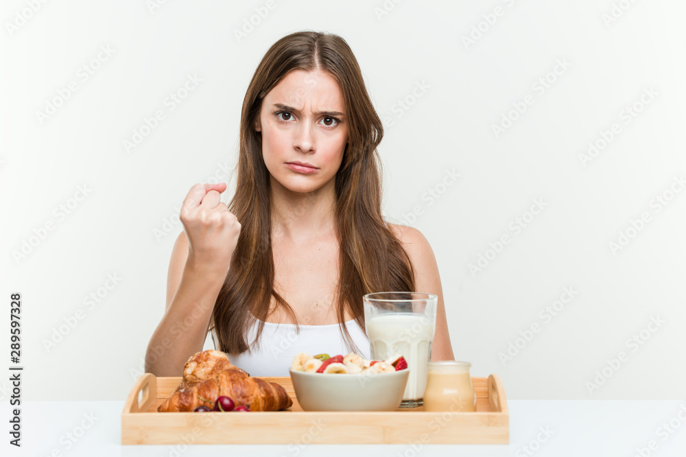 Young caucasian woman having breakfast showing fist to camera, aggressive facial expression. Young caucasian woman having breakfast showing fist to camera, aggressive facial expression.