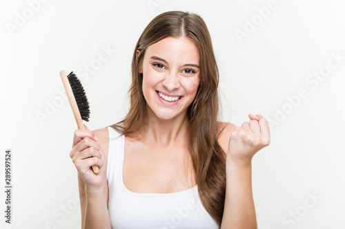 Young caucasian woman holding a hair brush cheering carefree and excited. Victory concept.