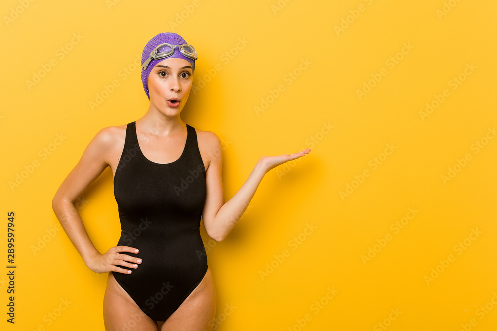 Young swimmer caucasian woman impressed holding copy space on palm.