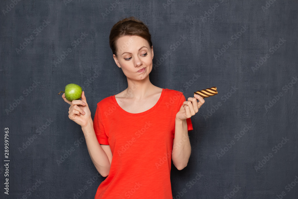 Doubting woman is making choice between apple and cookie Doubting woman is making choice between apple and cookie