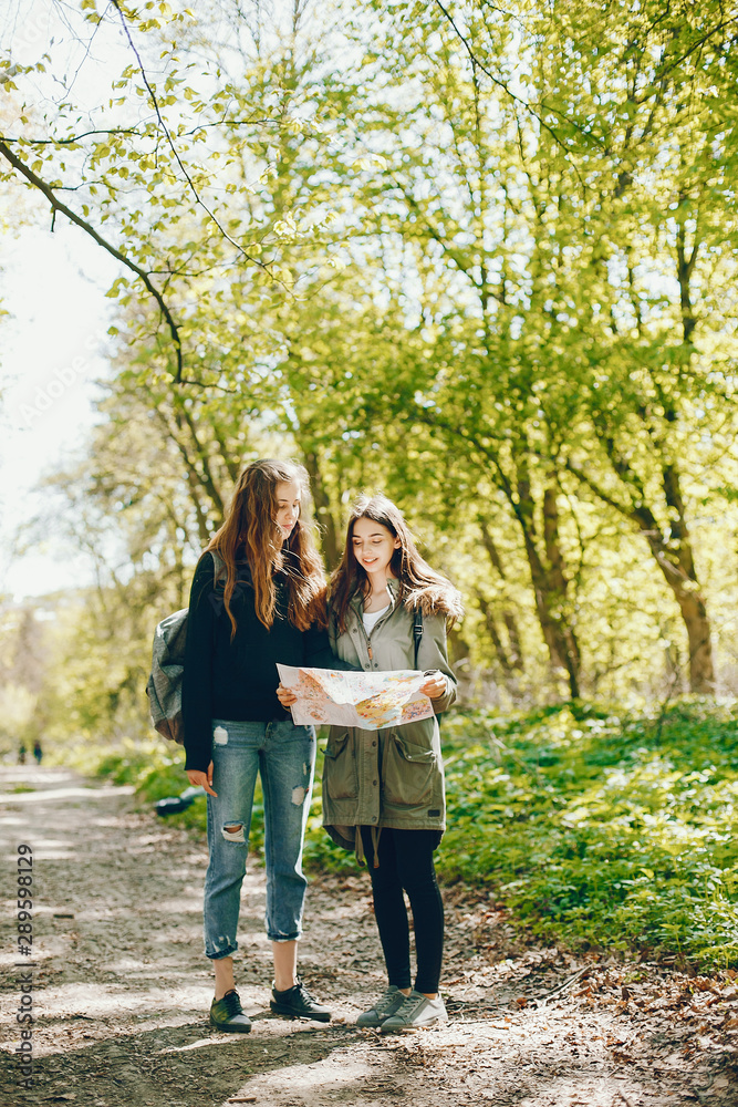 Two girls standing in a autumn forest. Friends have fun in a park. Tourists use the map.